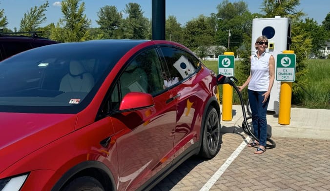 A person stands to a car plugged into an EV charger in a parking lot